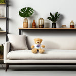 Customizable teddy bear on a white couch with a shelf of plants and jars in the background