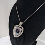 Customizable double-sided heart shaped silver rhinestone pendant with a silver necklace on a black stand