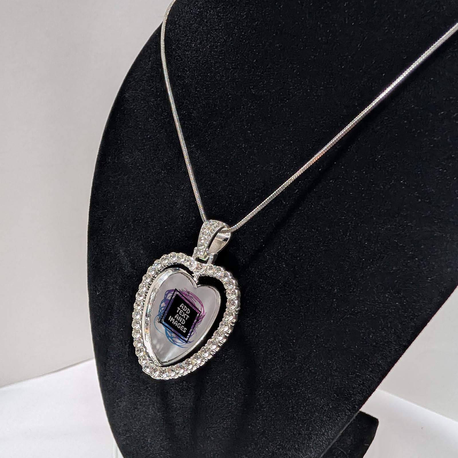 Customizable double-sided heart shaped silver rhinestone pendant with a silver necklace on a black stand