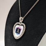 Customizable double-sided heart shaped silver rhinestone pendant with a silver necklace on a black stand