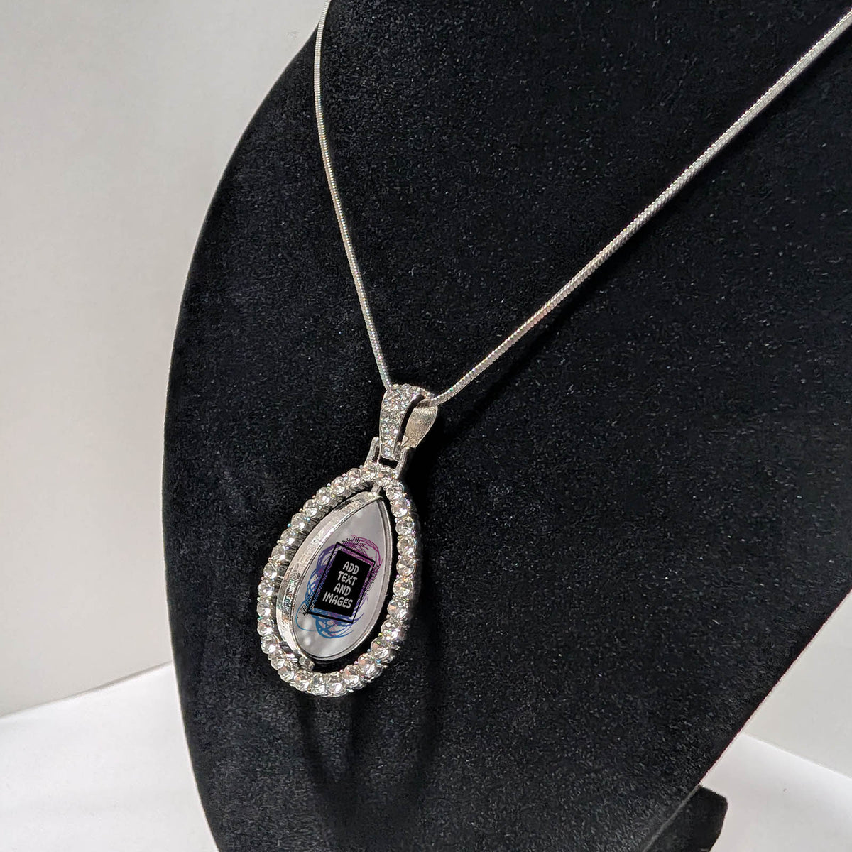 Customizable double-sided teardrop shaped silver rhinestone pendant with a silver necklace on a black stand