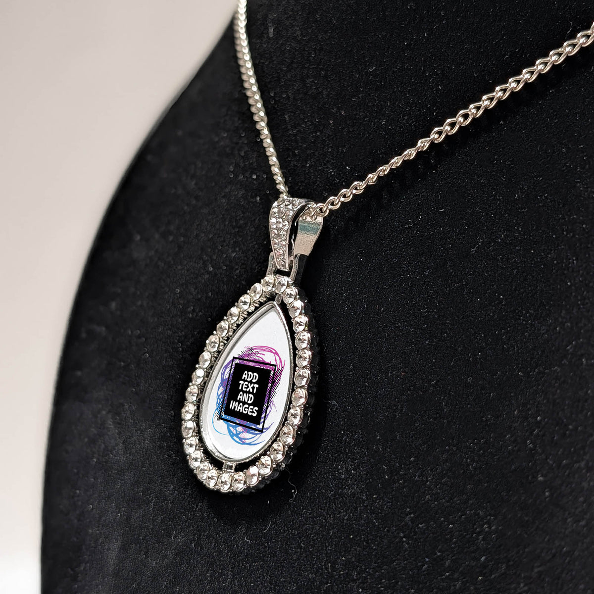 Customizable double-sided teardrop shaped silver rhinestone pendant with a silver necklace on a black stand