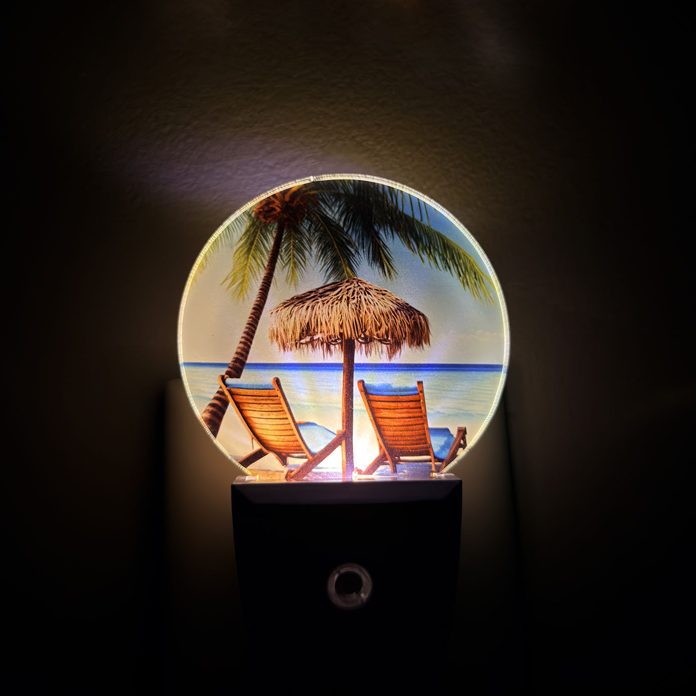 LED night light with a beach scene featuring palm trees, lounge chairs, and a hut on a dark background.