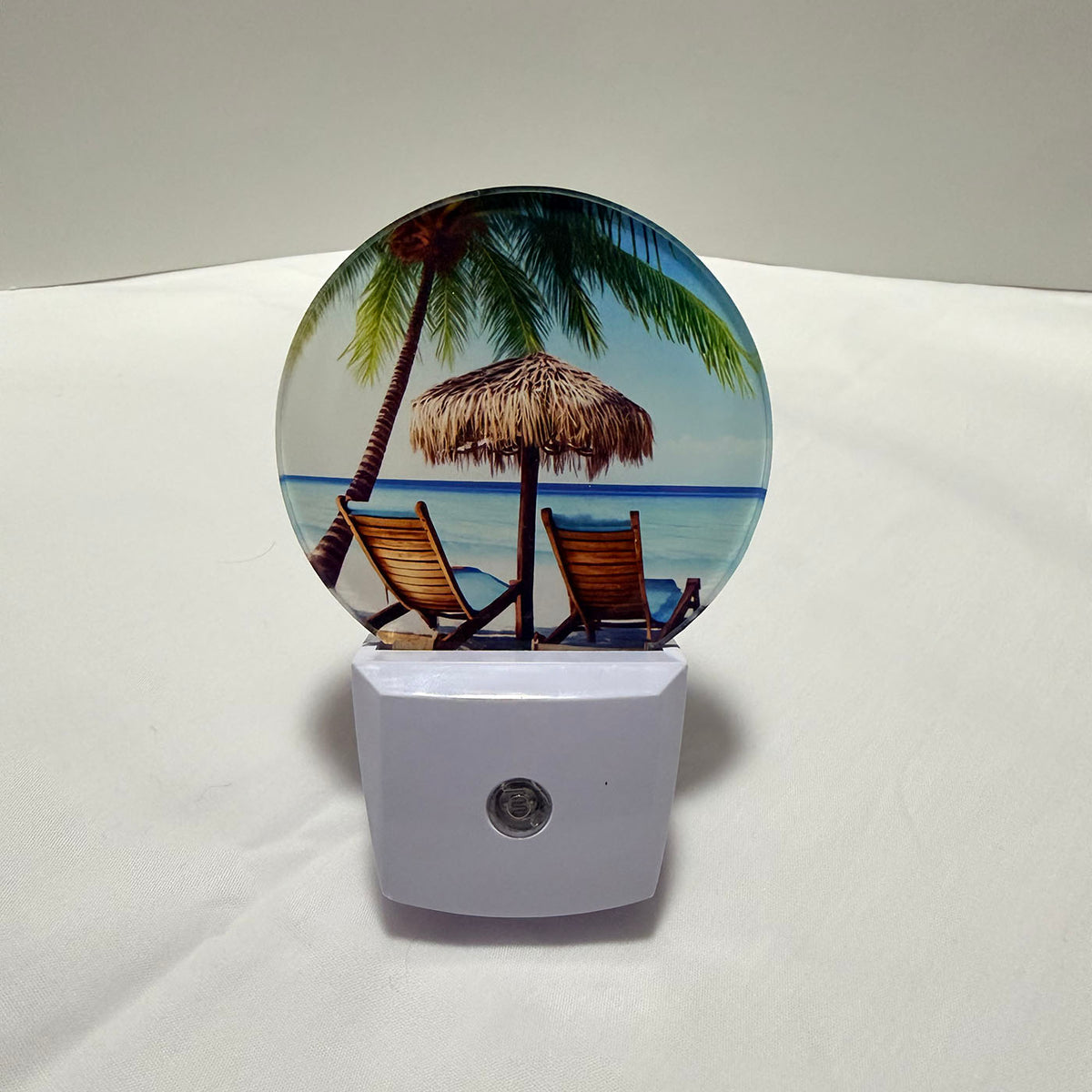 LED night light with a beach scene featuring palm trees, lounge chairs, and a hut on a dark background.