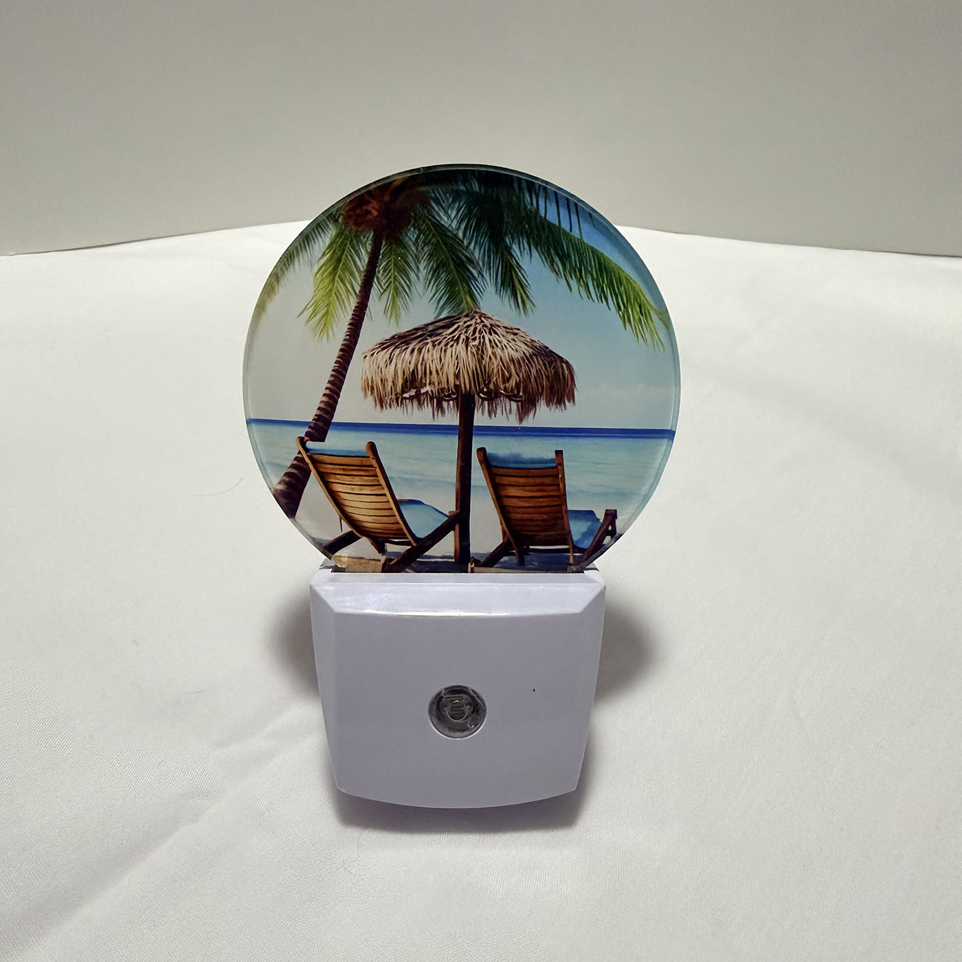 LED night light with a beach scene featuring palm trees, lounge chairs, and a hut on a dark background.
